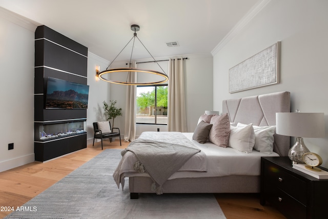 bedroom with ornamental molding, a large fireplace, an inviting chandelier, and light wood-type flooring