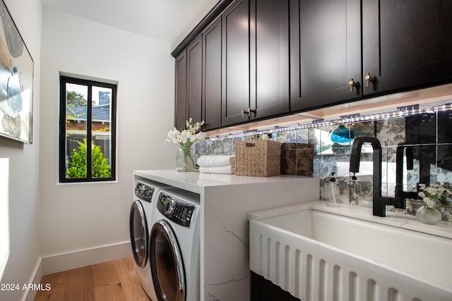 laundry area with cabinets, sink, washer and clothes dryer, and light hardwood / wood-style flooring