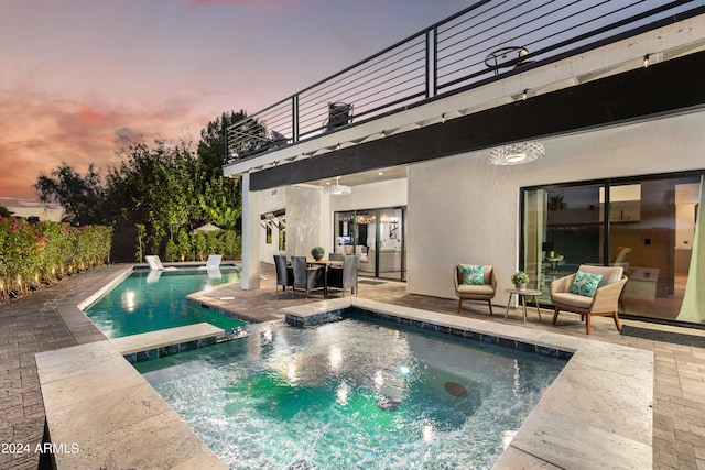 pool at dusk featuring a patio and an in ground hot tub