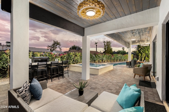 patio terrace at dusk featuring exterior bar, an outdoor living space, and a swimming pool with hot tub