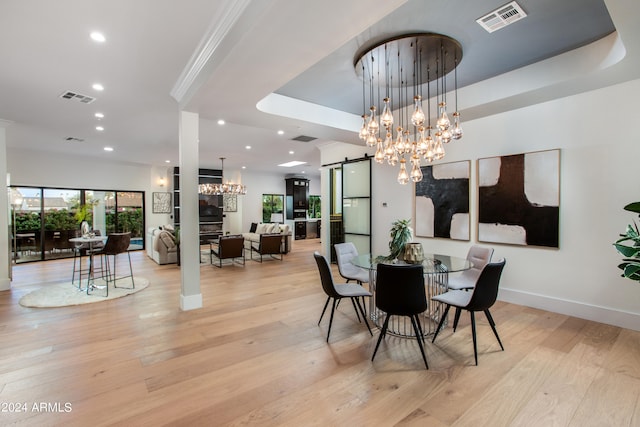 dining room with a barn door, a raised ceiling, light wood-type flooring, and an inviting chandelier