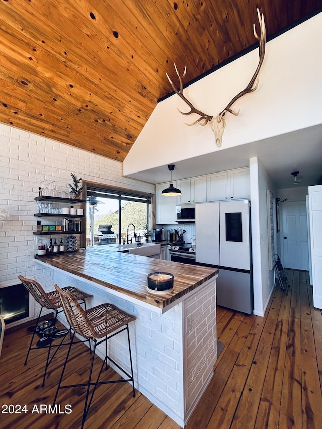 kitchen with dark wood-type flooring, white cabinetry, stainless steel appliances, hanging light fixtures, and a kitchen breakfast bar