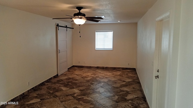 spare room featuring ceiling fan and a barn door