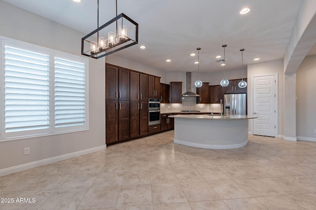 kitchen with light stone counters, decorative light fixtures, stainless steel appliances, an island with sink, and wall chimney exhaust hood