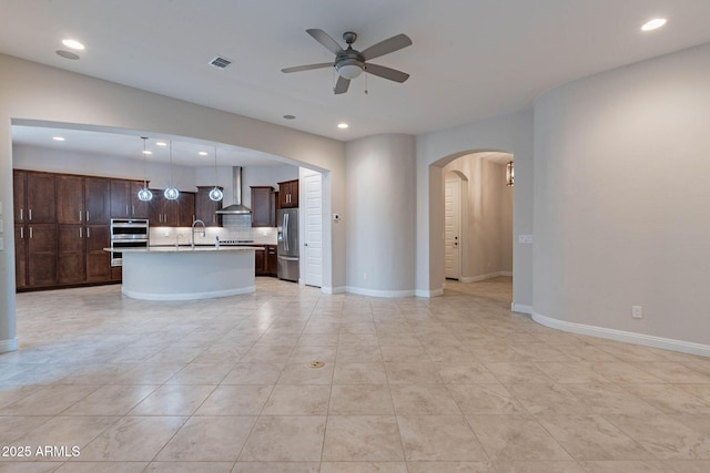 unfurnished living room featuring a ceiling fan, baseboards, arched walkways, and a sink