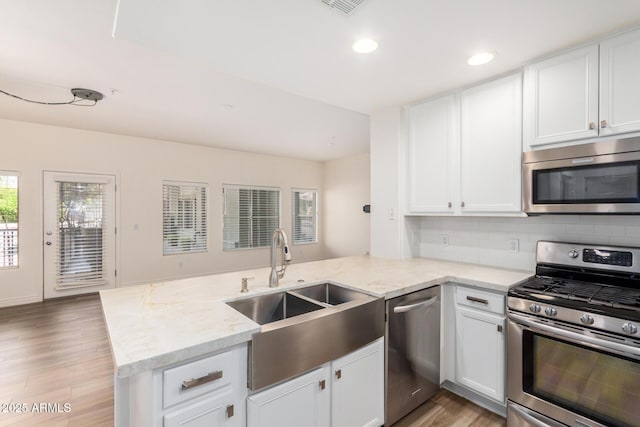 5450 E Deer Valley Dr Unit 1211, Phoenix, AZ 85054 - kitchen with stainless steel appliances, a peninsula, white cabinetry, light wood-type flooring, and decorative backsplash