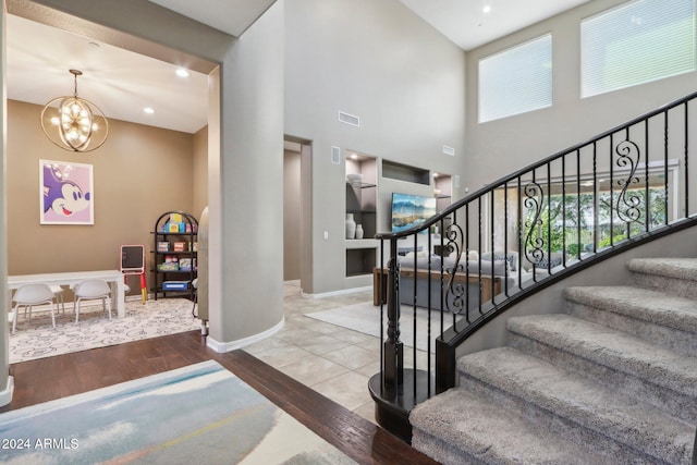 stairway with an inviting chandelier, a towering ceiling, wood-type flooring, and plenty of natural light