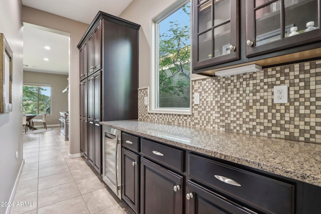 kitchen with dark brown cabinetry, light tile patterned flooring, wine cooler, light stone counters, and backsplash