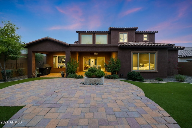 back house at dusk with a lawn and a patio area