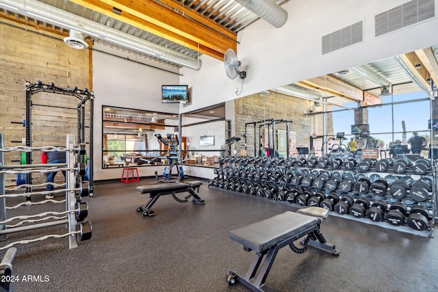 exercise room with a towering ceiling and brick wall