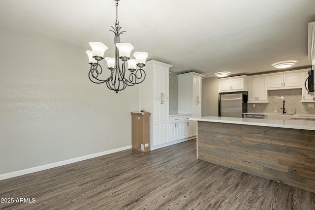 kitchen with baseboards, dark wood-style flooring, freestanding refrigerator, light countertops, and backsplash