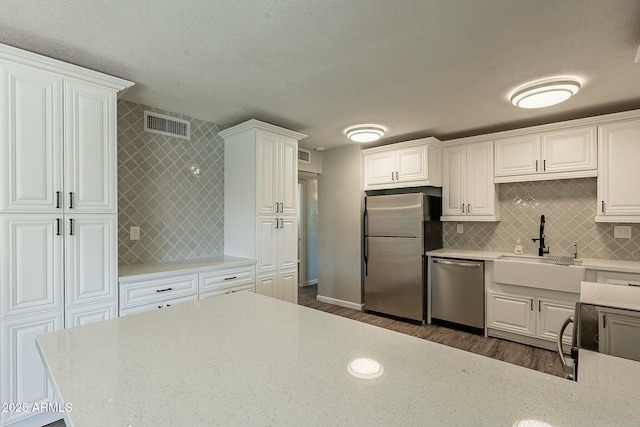 kitchen with stainless steel appliances, tasteful backsplash, a sink, and white cabinets