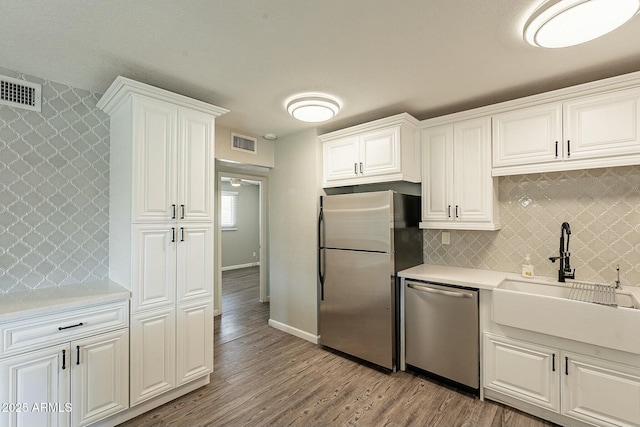 kitchen featuring light wood finished floors, stainless steel appliances, light countertops, visible vents, and a sink