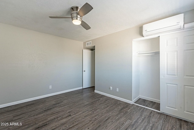 unfurnished bedroom featuring dark wood-type flooring, visible vents, baseboards, and a wall mounted AC