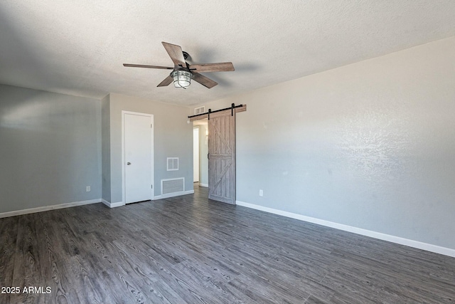 unfurnished bedroom featuring a barn door, dark wood-style flooring, visible vents, and baseboards