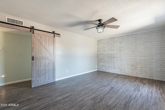 empty room featuring dark wood finished floors, visible vents, a barn door, ceiling fan, and a textured ceiling