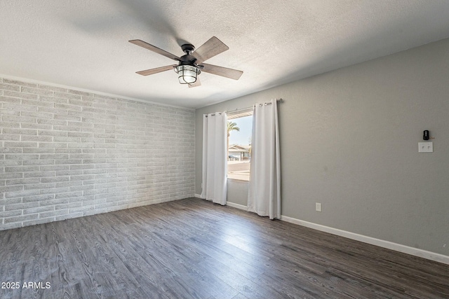 spare room with a textured ceiling, brick wall, a ceiling fan, baseboards, and dark wood finished floors