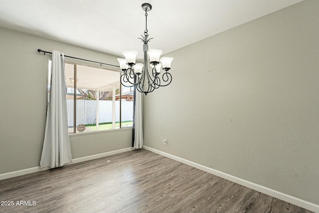 unfurnished room featuring baseboards, a chandelier, and wood finished floors