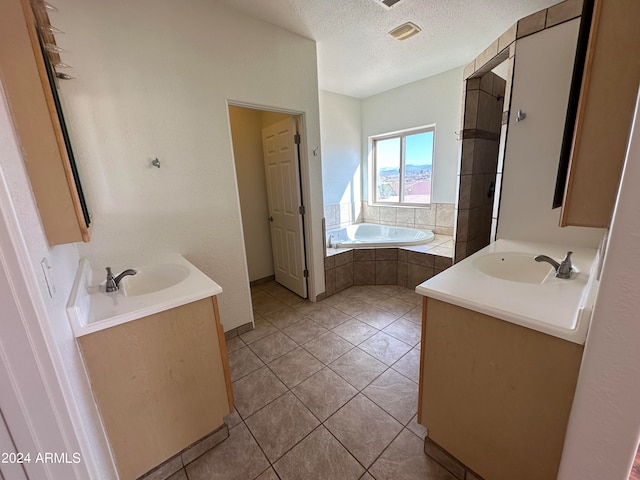 bathroom with tiled tub, vanity, a textured ceiling, and tile patterned flooring