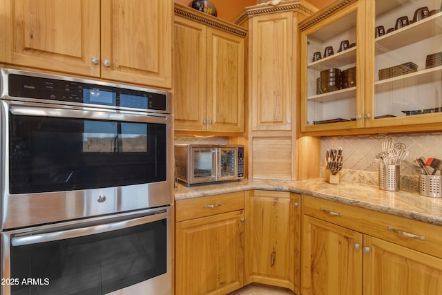 kitchen with stainless steel double oven, glass insert cabinets, light stone countertops, and tasteful backsplash