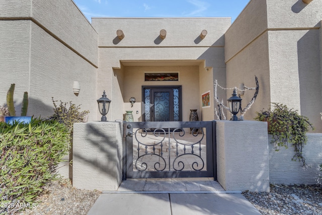 doorway to property with a gate, stucco siding, and fence