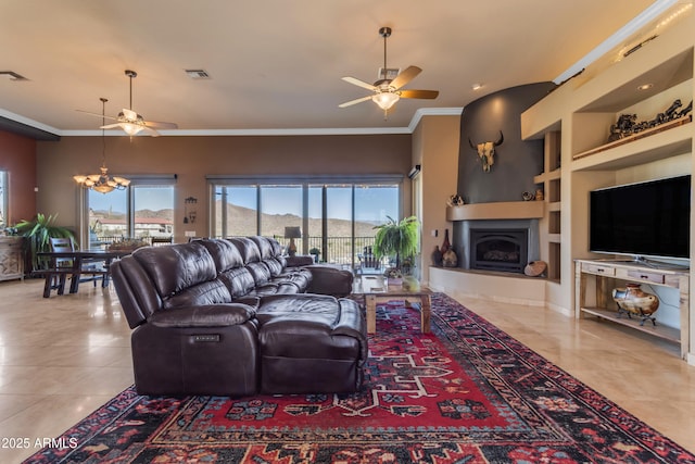 tiled living area featuring ornamental molding, built in features, ceiling fan with notable chandelier, and a fireplace with raised hearth