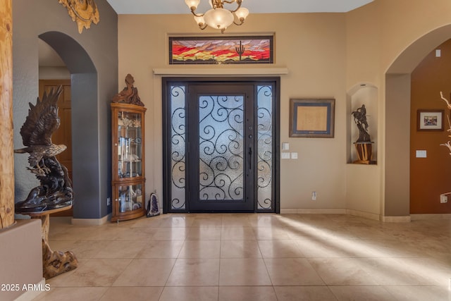 foyer featuring tile patterned flooring, baseboards, arched walkways, and a chandelier