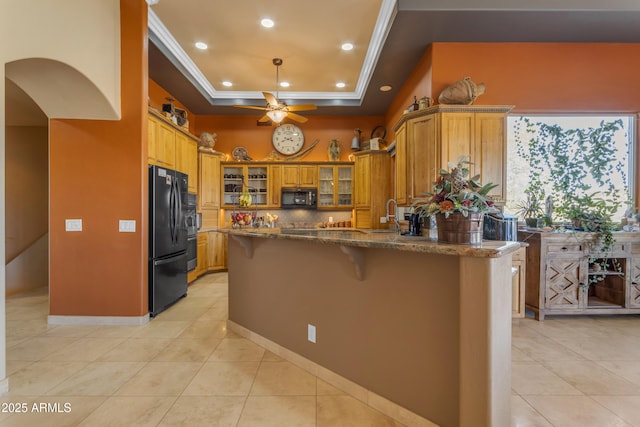 kitchen with a tray ceiling, brown cabinets, a kitchen breakfast bar, a peninsula, and black appliances