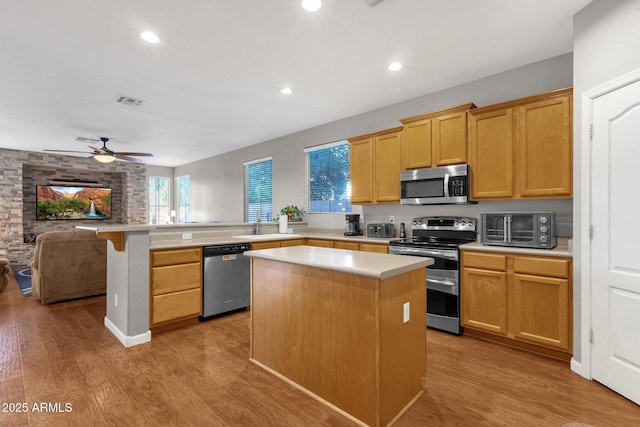 kitchen featuring light hardwood / wood-style floors, kitchen peninsula, ceiling fan, appliances with stainless steel finishes, and a kitchen island