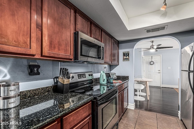 3825 E Camelback Rd Unit 152, Phoenix, AZ 85018 - kitchen featuring appliances with stainless steel finishes, arched walkways, a ceiling fan, light tile patterned floors, and dark stone counters
