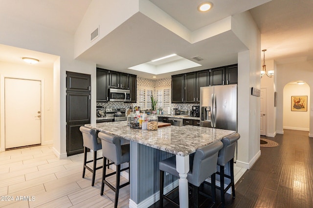 kitchen with appliances with stainless steel finishes, light hardwood / wood-style floors, decorative backsplash, a kitchen bar, and a center island