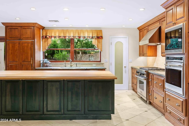 kitchen with light tile patterned floors, appliances with stainless steel finishes, sink, wall chimney range hood, and wooden counters