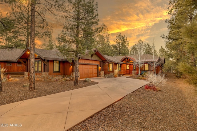 rustic home with an attached garage, stone siding, and concrete driveway