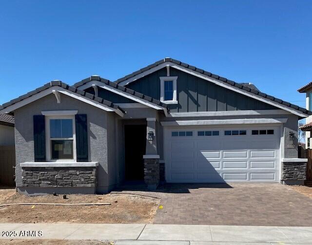 craftsman inspired home featuring decorative driveway, a tile roof, stone siding, and board and batten siding