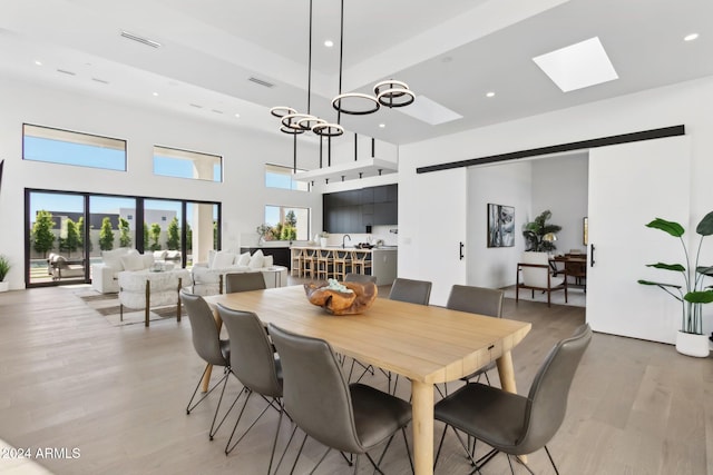 dining area featuring a notable chandelier, light wood-type flooring, a towering ceiling, and a skylight