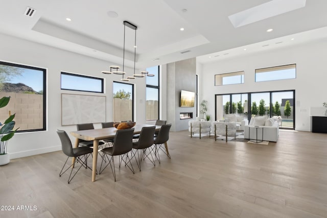 dining room featuring a chandelier, a large fireplace, a tray ceiling, and light hardwood / wood-style flooring