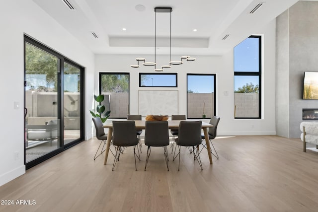 dining area with a raised ceiling, a tiled fireplace, and light hardwood / wood-style flooring