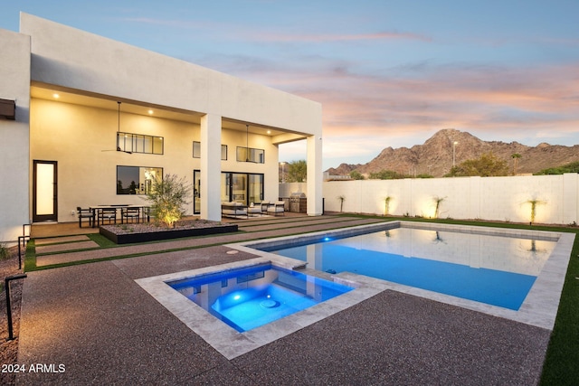 pool at dusk featuring an outdoor living space with a fire pit, an in ground hot tub, a mountain view, and a patio