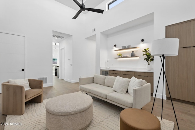 living room with ceiling fan, light hardwood / wood-style flooring, and a high ceiling