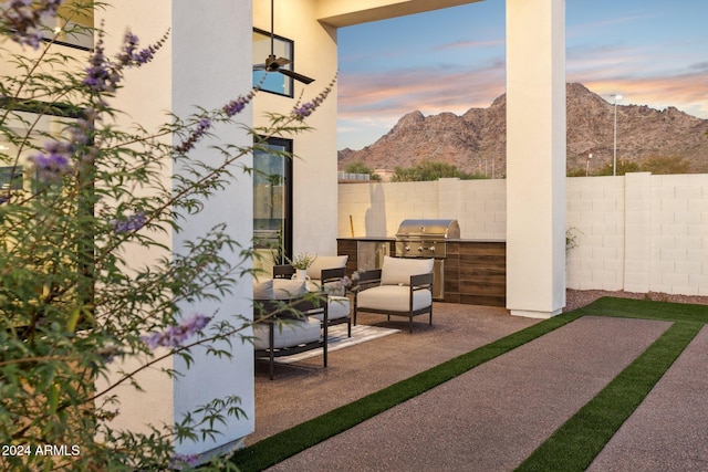 patio terrace at dusk with a grill, a mountain view, and an outdoor kitchen