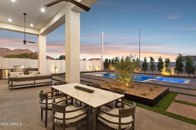 patio terrace at dusk with area for grilling, a mountain view, and a pool with hot tub