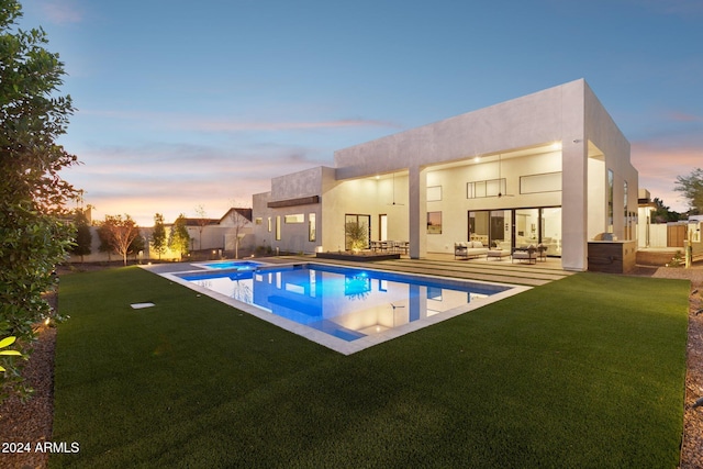 pool at dusk with an in ground hot tub, an outdoor living space, a patio area, and a lawn