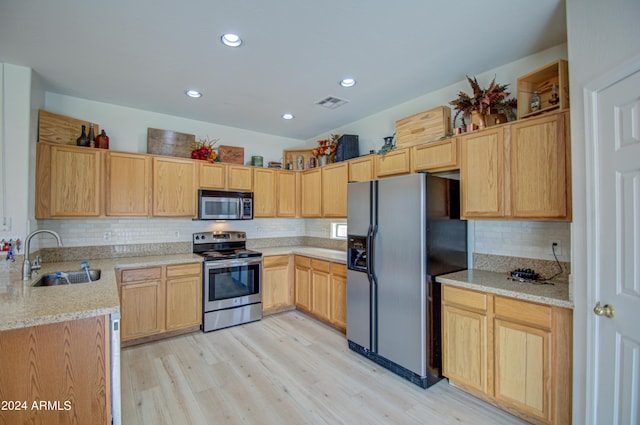 kitchen with appliances with stainless steel finishes, sink, light stone counters, light brown cabinets, and light hardwood / wood-style flooring