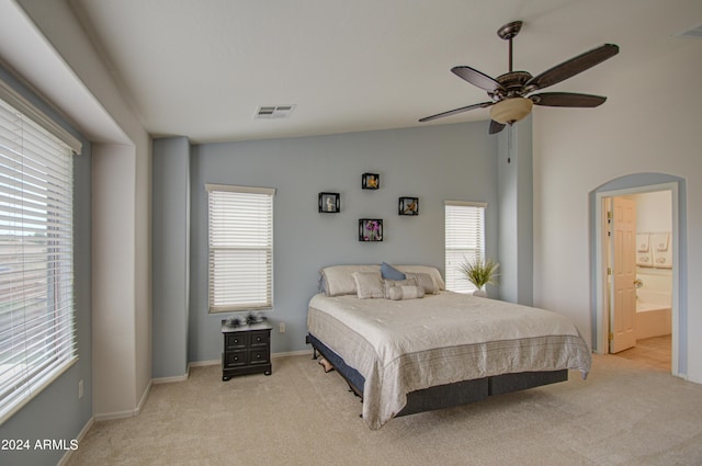 bedroom featuring lofted ceiling, ensuite bath, light colored carpet, and ceiling fan