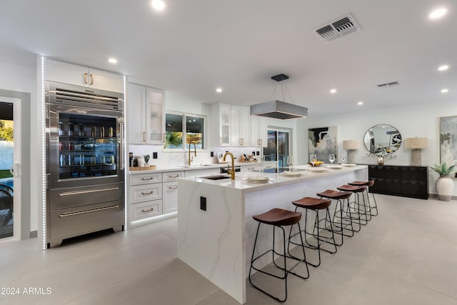 kitchen featuring light stone countertops, wall oven, a kitchen island with sink, sink, and white cabinets