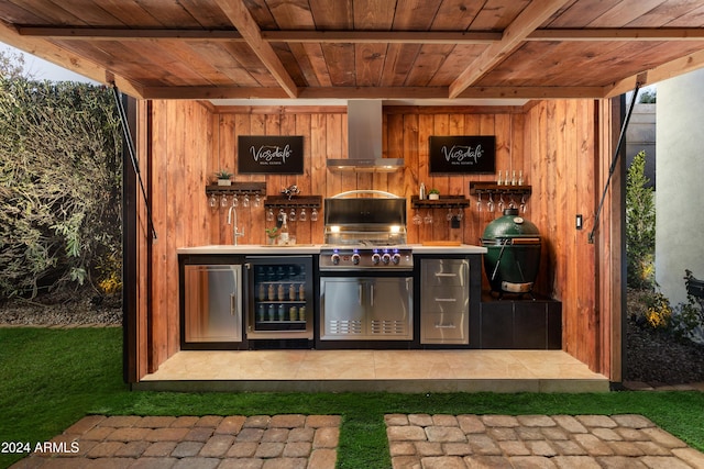 bar with a wealth of natural light, beverage cooler, wood walls, and wall chimney range hood