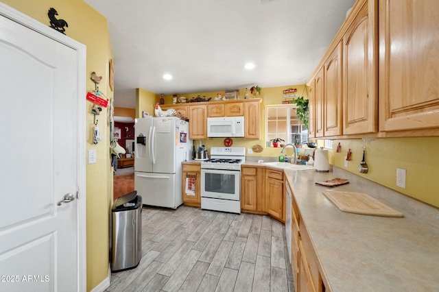 kitchen with light wood finished floors, light countertops, light brown cabinetry, a sink, and white appliances
