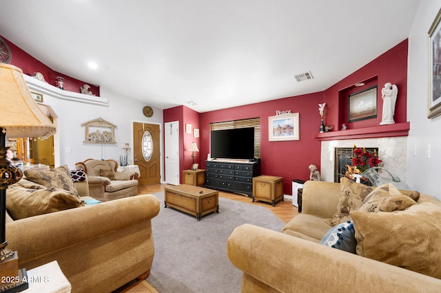 living area with visible vents, a tiled fireplace, and wood finished floors