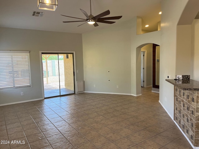 spare room featuring arched walkways, ceiling fan, a high ceiling, visible vents, and baseboards