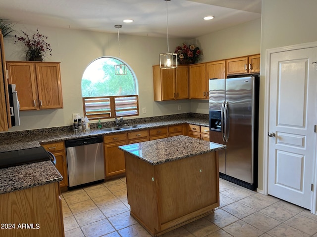 kitchen featuring a center island, stainless steel appliances, brown cabinetry, a sink, and dark stone counters